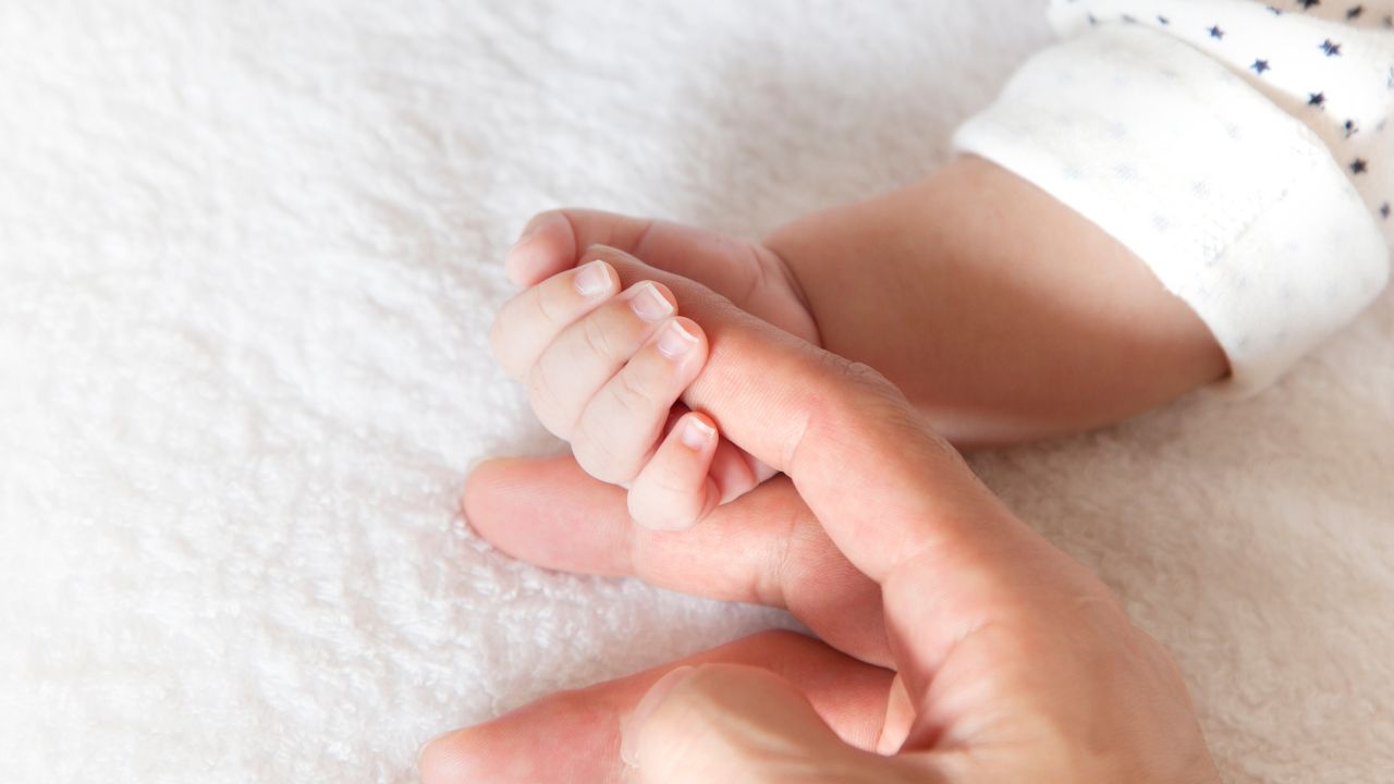 新生児の小さな手を握る大人の指。妊娠中の栄養管理が赤ちゃんの健康な成長につながることを表現したイメージ