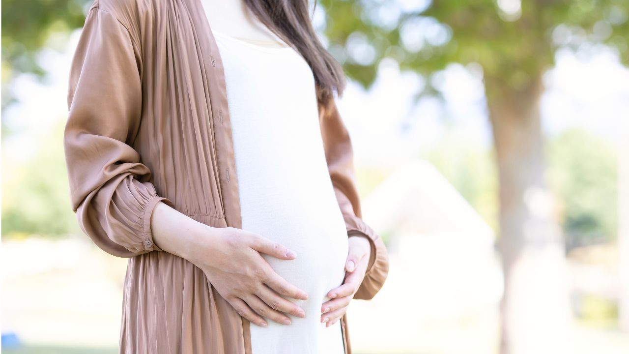 屋外でお腹を優しく抱える妊婦。妊娠中から意識したい赤ちゃんの鉄分補給と母体の栄養管理